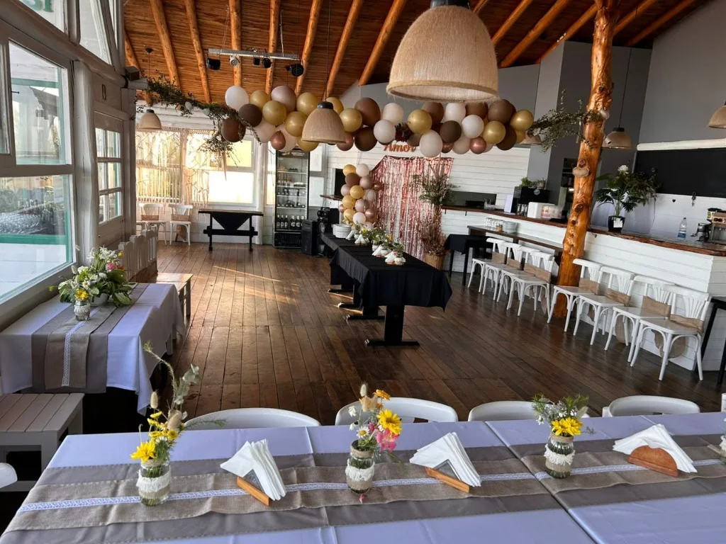 Salón vidriado de Playa 13 decorado con guirnaldas de globos, flores y mesas vestidas